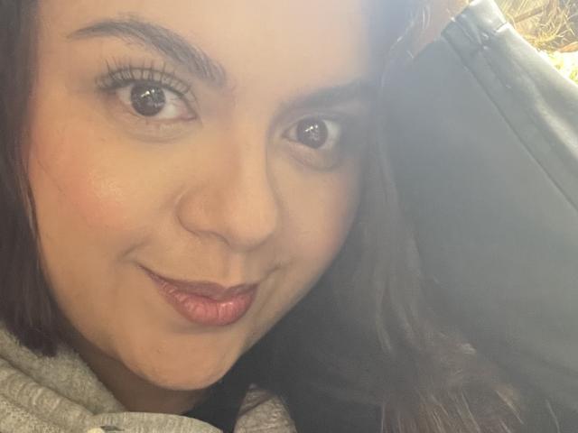 MissSofiia's face, pouty lips, brown eyes, and dark hair, wearing a gray hoodie, with a slight smirk, light blush on her cheeks, and subtle makeup.