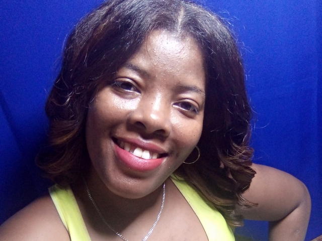 BrownieBabe has dark brown, curly hair, and a shiny, happy smile with red lipstick. She's wearing a yellow top and a silver necklace. Her ass is not visible.