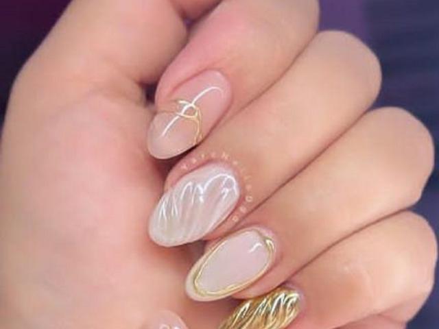 LinsayColemann's hand with nude nails, gold wire designs, and white wavy patterns on the index and middle fingers. Her nails are glossy and well-manicured.