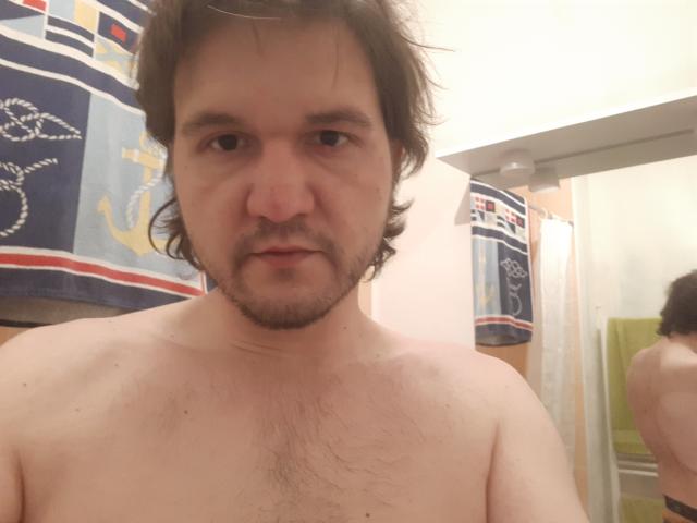 NectarineFad is a shirtless dude with medium brown hair, a beard, and chest hair, standing in front of a mirror, showing a reflection of his back.