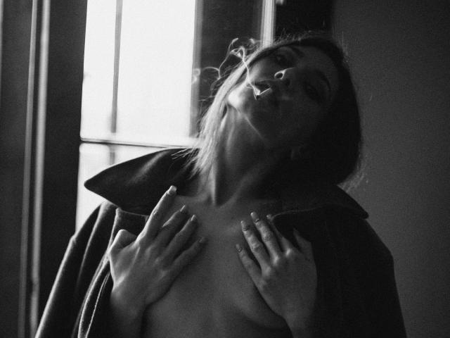 MoniFoxy with her eyes closed, head tilted back, wearing an open jacket, hands covering her tits, in a black-and-white photo. Her lips are slightly parted.