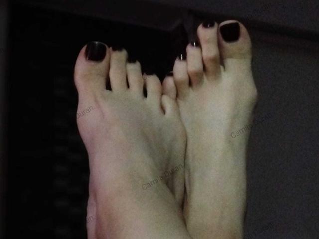 Les pieds d'AbbyCollings, avec des ongles des orteils d'un violet foncé, les orteils pointés vers le haut, montrant la plante de ses pieds et ses orteils dans une photographie légèrement floue et sombre..