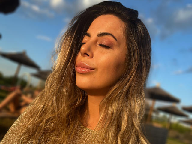 VictoriaModel with her eyes closed, soft smile, and wavy blonde hair, wearing a shiny brown sweater, sunlit skin, and subtle pink eyeshadow. Her ass is not visible.
