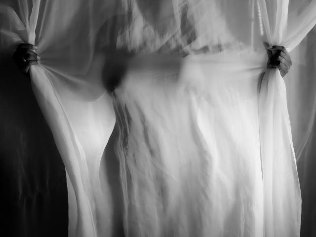 LizHerrera's hands gripping white curtains, revealing her bare chest and small, perky tits through the semi-transparent fabric, in a black-and-white, slightly blurred image.