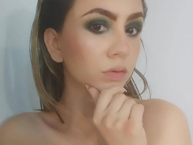 KariCarter ha un trucco occhi verde scuro, sopracciglia marroni, capelli umidi e una mano vicino alla bocca con un'espressione pensierosa. Il suo seno è leggermente visibile, è nuda..