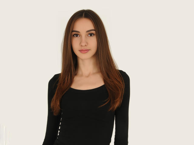 VioletaAndLeo has long brown hair, a black long-sleeve top, and a cute face with brown eyes and pink lips. She's standing against a plain white background.