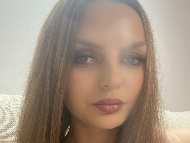 DouceAmelia has long brown hair, full eyebrows, and glossy pink lips. She's looking directly at the camera with subtle, sexy makeup and a slightly parted, seductive mouth.