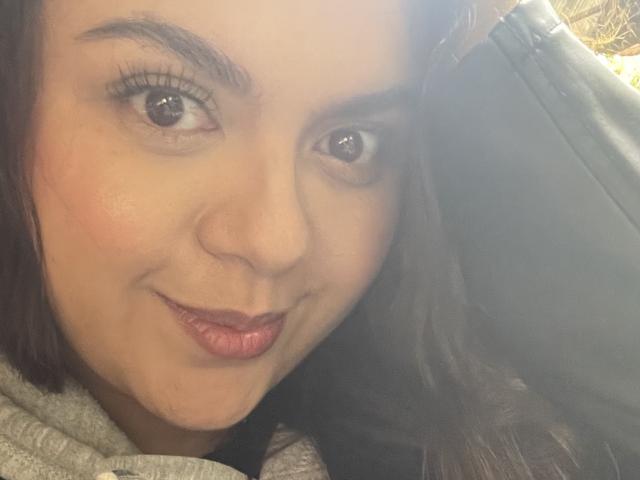 MissSofiia's face, showing her cute pout with slightly puckered red lips, brown eyes, and dark brown hair, wearing a gray hoodie, looking up with a subtle smile.