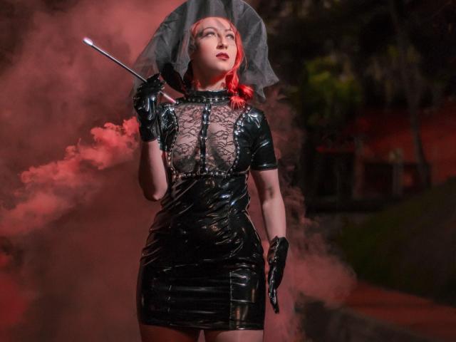 LauraDante em um vestido preto de látex brilhante com renda, segurando um chicote, usando luvas pretas e um guarda-chuva transparente, fumaça vermelha ao redor, cabelo ruivo, olhando para cima..