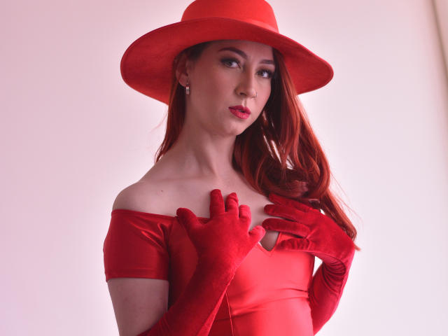 LauraDante with red hat, off-shoulder red dress, and red gloves, covering her small tits with her hands, has red lipstick and long red hair, looking sexy.