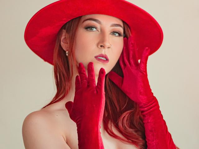 LauraDante with red velvet hat, red velvet gloves, and red lipstick, touching her face with red-gloved hands, showing her pale skin and green eyes.