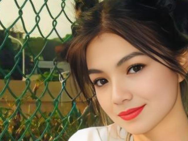 SmileDiana has dark brown hair, red lipstick, and black eyeliner, with a green chain-link fence in the background. Her ass is not visible, just her face.