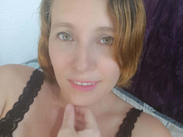 CharlottePonze with short brown hair, green eyes, and a cute smile, wearing a black lace bra, touching her chin. She's got a slight tan and pink lips.