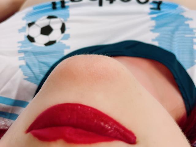 MelanieFrancaiseDuo, con una marca de beso de lápiz labial rojo en su labio superior, vistiendo una camiseta de fútbol con un patrón azul y blanco y un logo de pelota de fútbol..