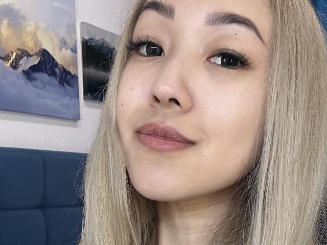 Het gezicht van RenyLime, met blond haar en lichtjes opgetrokken, roze lippen, lange wimpers en subtiele make-up. Haar bruine ogen kijken iets naar rechts. Ze glimlacht subtiel..