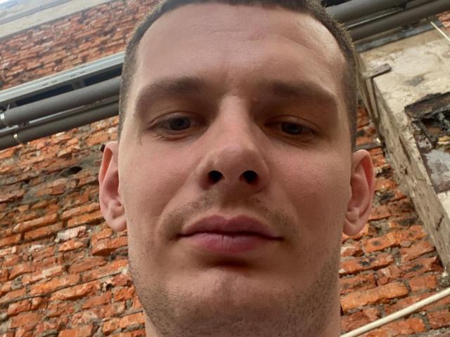 AngelaAndConnie's face, short brown hair, slight stubble, small nose, slight smile, brown eyes, looking directly at camera, brick wall in background.