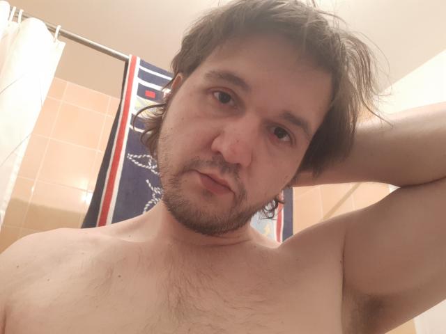 NectarineFad, shirtless with chest hair, brown wavy hair, and beard, looking at camera with hand behind head, in bathroom, showing armpit.