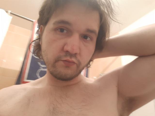 NectarineFad is a shirtless dude with brown hair, a beard, and hairy chest, looking at the camera with a slight smile, raising his arm behind his head.