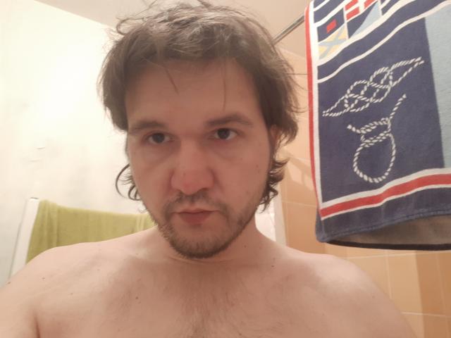 NectarineFad is a shirtless, middle-aged man with messy brown hair, a beard, and a slightly annoyed expression. His chest is hairy. A blue towel with a white design hangs.