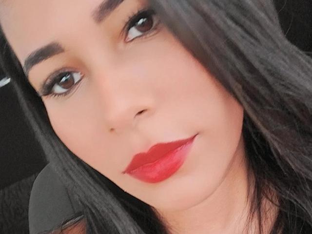 AnandaHot has smooth brown skin, dark eyebrows, long black hair, and red lipstick. Her eyes are looking slightly upwards with a subtle smile.