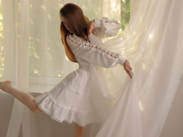 MiaBerry in a white lace dress, lifting her skirt, exposing her bare ass, her long brown hair flowing, holding a sheer curtain, sunlight filtering through.