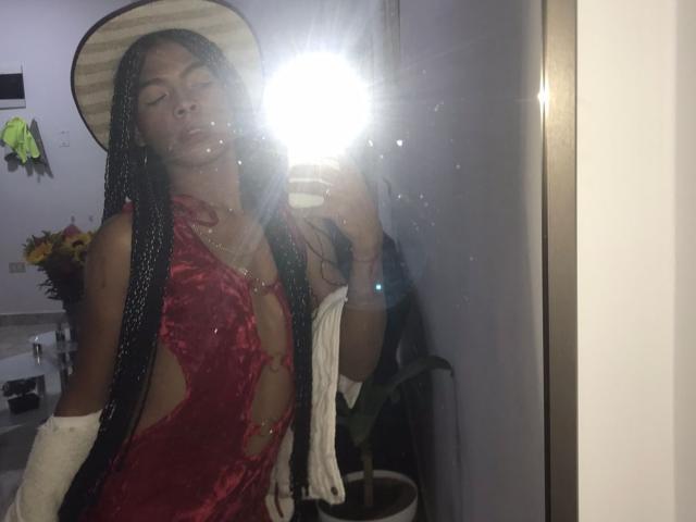 BriyitTs in a red, cut-out dress with visible tits, wearing a cowboy hat and white gloves, taking a selfie in a mirror, flash obscuring face.