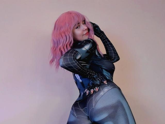 RonyTight with pink wavy hair, wearing a tight black Spider-Man suit, showing her curvy ass and small tits, smiling and touching her face.