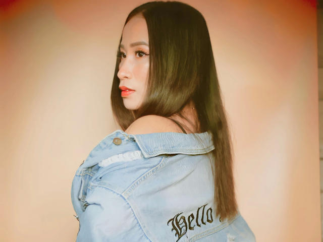 OHCUMTOMYTITS-hot with long brown hair, wearing a blue denim jacket, looking over her shoulder, red lipstick, soft brown eyes, and a slightly open mouth.