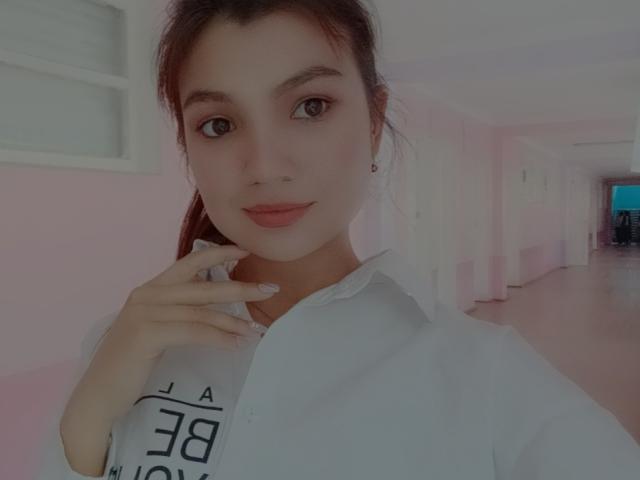 SmileDiana has light skin, red hair in a ponytail, and is wearing a white shirt with a hand near her chin. She has pink lipstick and is looking at the camera.