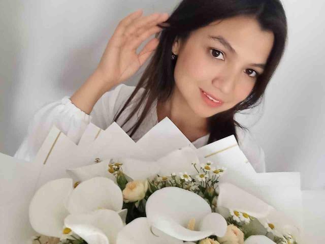 SmileDiana with long black hair, white blouse, holding bouquet of white flowers and small yellow roses, smiling, right hand touching hair. Soft pink lips, light makeup, cute.