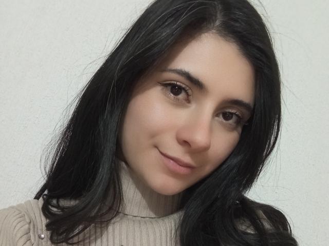 JeneKurz has long black hair, brown eyes, and a slight smile. She's wearing a beige ribbed turtleneck, and her face is fair with a cute, relaxed look.