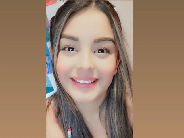 TalianaSquirt has light skin, brown eyes, long brown hair, and a cute smile with pink lipstick. She's looking at the camera with a friendly, relaxed expression.