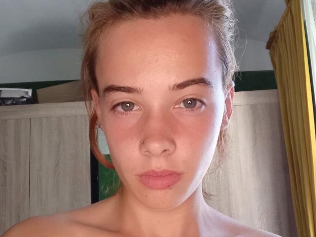 EvieEve has a cute face with green eyes, a small nose piercing, and pink lips. She's topless, with brown hair tied back, looking straight at the camera.