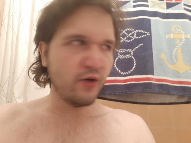 Blond-haired NectarineFad with slightly messy hair, bare chest, and an open mouth, looking to the side in a blurry bathroom selfie.
