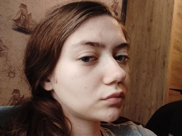 Svetik69 has pale skin, brown eyes, and brown hair in a ponytail. Her nose is slightly upturned with a small, almost invisible boogers. She looks bored with a slight pout.