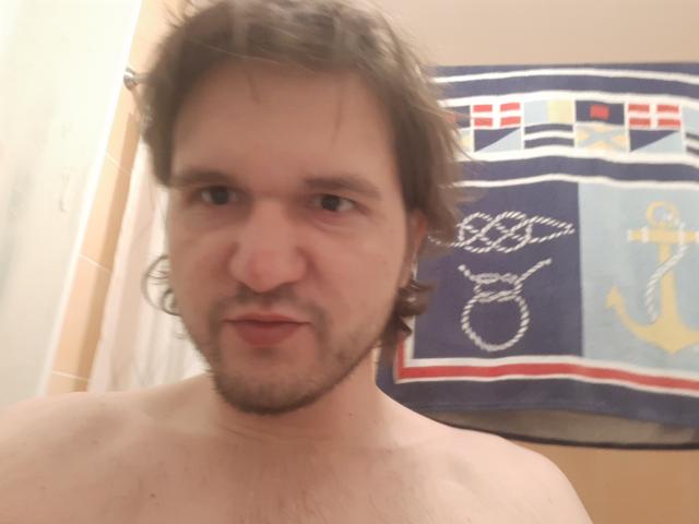 NectarineFad is a shirtless guy with messy brown hair, a beard, and a slight smile, showing a bit of chest hair. His eyes are half-closed, and he looks relaxed.