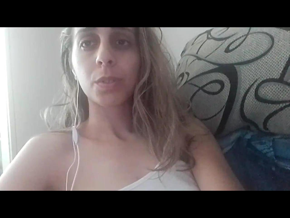 VanessX has a tired, slightly open-mouthed expression, wearing a white tank top, with blonde, wavy hair and a visible earbud in her right ear.