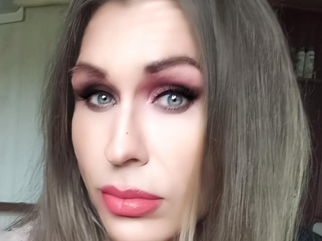 LilianaShe has pale skin, blue eyes, pink eyeshadow, thick black eyelashes, pink lipstick, and straight grayish-brown hair. She's looking at the camera with a neutral expression.