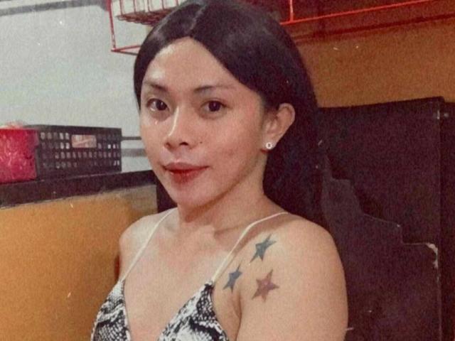 SuckableMistress - uma mulher atraente com cabelo preto, seios pequenos, tatuagens de estrelas no ombro, vestindo um vestido estampado, sorrindo, batom vermelho, brincos e uma pequena perfuração no nariz, em um ambiente casual..