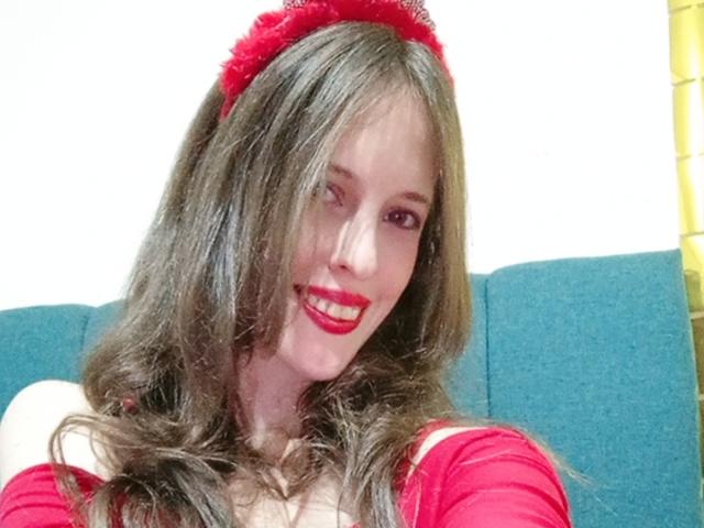 AlissonS69 has long brown hair, red lipstick, and a red headband. She's smiling with red makeup and a red top, showing her tits. She's sitting on a blue couch.