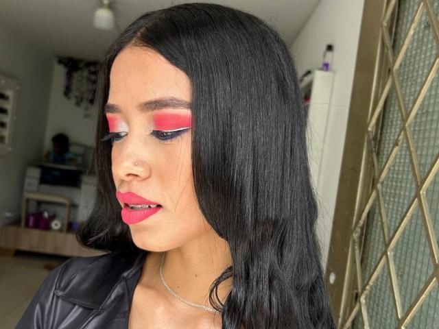 LaurentRay with black hair, pink eyeshadow, red lipstick, black leather jacket, nose piercing, and silver necklace, looking down. Boobs are not visible.