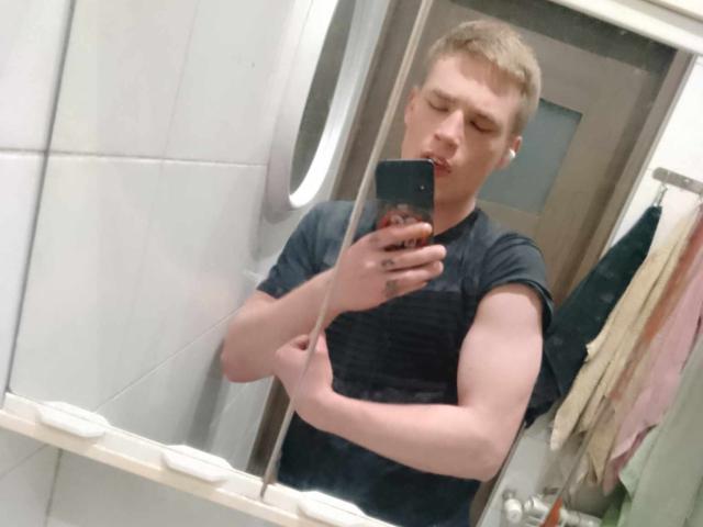 WarzyWkawcipce with short blonde hair, pouty lips, and a black t-shirt, holding a phone, taking a mirror selfie, showing a muscular, tattoo-free arm.