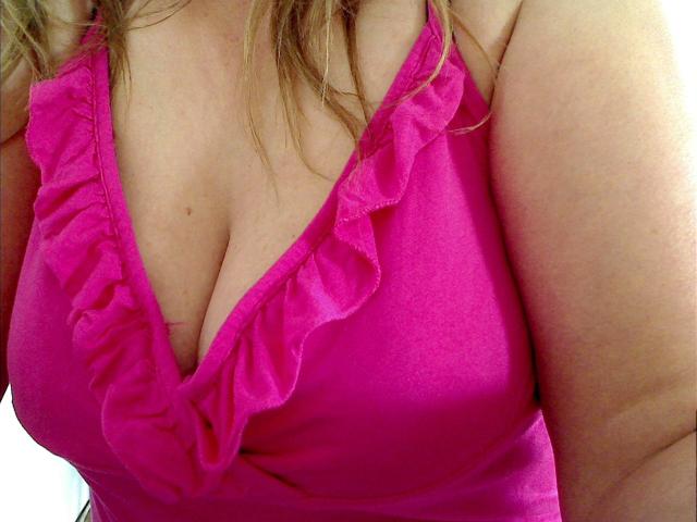 Lissy-Privat-hot's pink ruffled top, showing her large, plump boobs with a visible cleavage. Her blonde hair is partially in frame, and her arm is on the right.