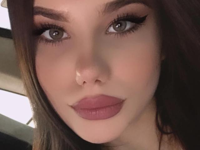 NicoleNight has puffy pink lips, a nose piercing, and thick black eyeliner with long lashes. Her brown eyes and straight brown hair are visible in the image.