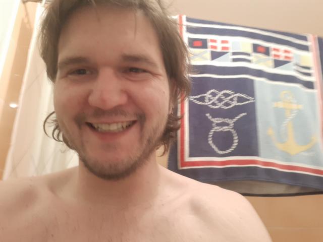 NectarineFad is a shirtless dude with a happy face, brown wavy hair, and a beard. His blue and white nautical towel is in the background.