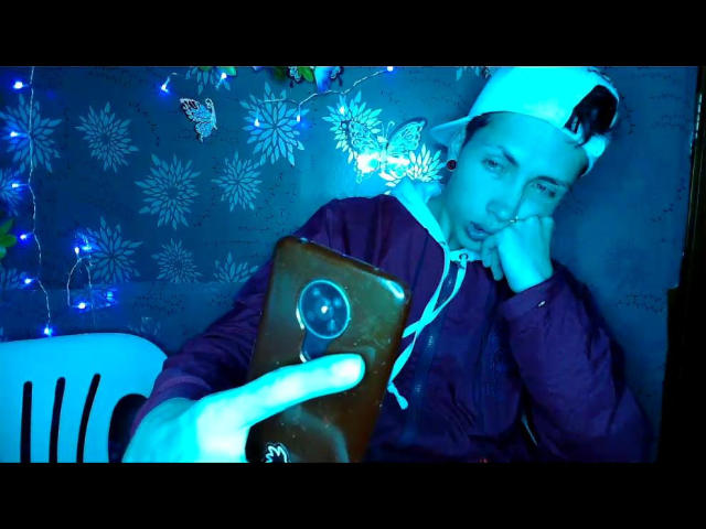 PuccaGaru69 with a blue-tinted face, wearing a white cap, purple hoodie, and holding a brown phone, taking a selfie, with a hand on their chin, looking bored.