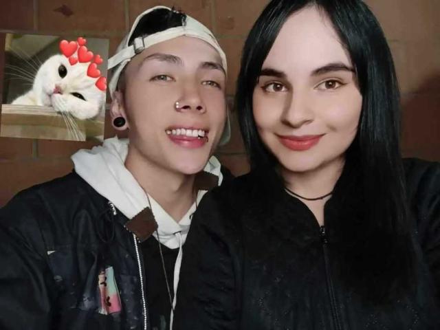 PuccaGaru69 with black hair, red lipstick, and black jacket, next to PuccaGaru69 with white headband, nose ring, and black jacket, showing teeth, with a chicken in background.