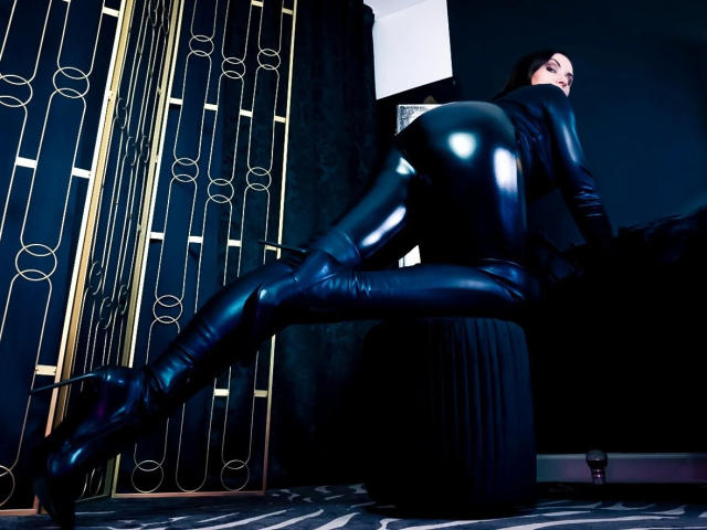 LongetsLegs-hot in black latex outfit, shiny boots, crouching with ass raised, looking back. Black room with gold-patterned screen and black curtain. High heels, latex texture.