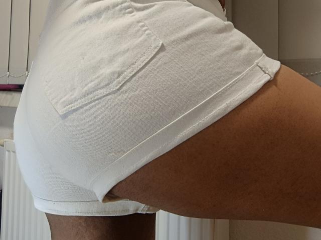 Paty69s' white butt shorts are tight around their brown butt, showing a small pocket and fraying at the edge. Paty69s is standing with one leg raised.