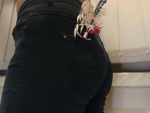 Paty69s's ass in tight black jeans, back pocket with white, purple, and red flowers sticking out. Paty69s's butt is prominent, jeans are slightly worn, metal buttons visible.